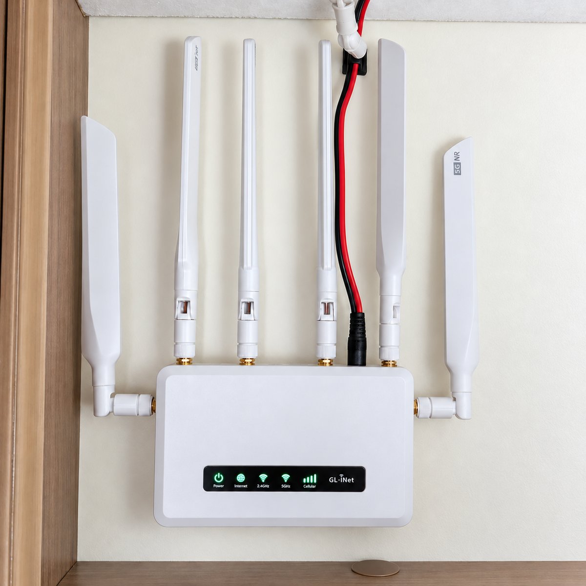 A white GL.iNet Spitz AX router with six aerials, mounted inside a motorhome cupboard, with its red and black 12V power lead running up to the ceiling and its status lights showing a full mobile signal.